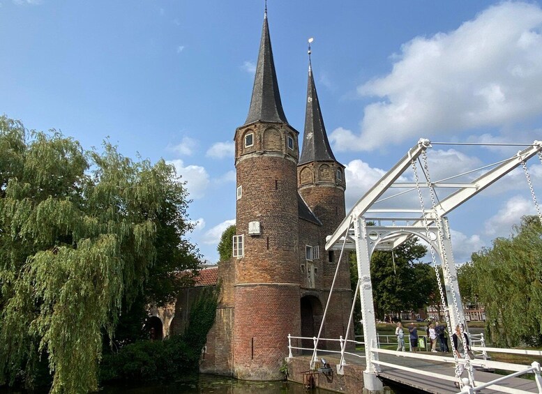 A historic brick tower with two spires, a white metal bridge, and willow trees. 5