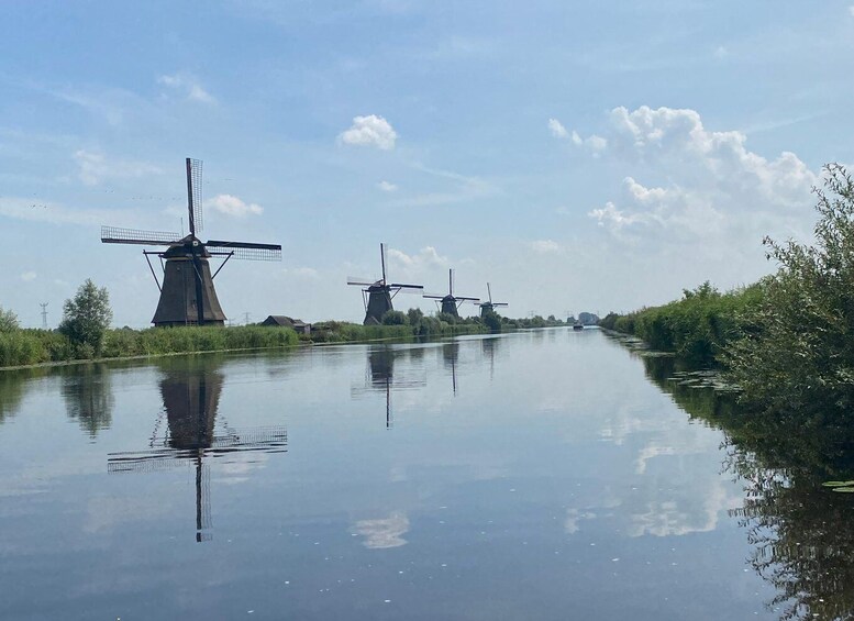 A canal with three windmills on the left bank, surrounded by greenery and calm water. 4