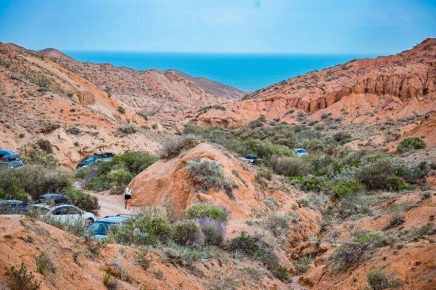 A rugged landscape with red rock formations, a clear blue sky, and a distant view of the ocean. 4