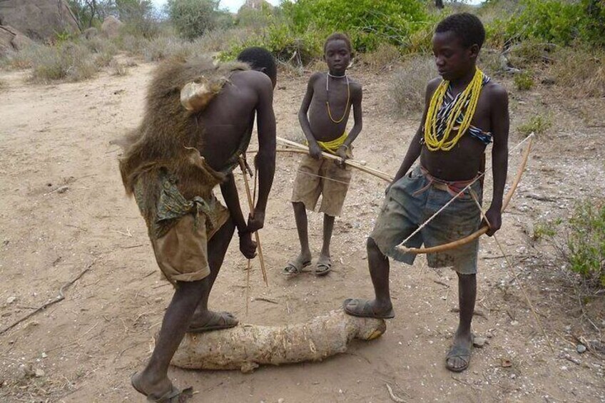 Three men with a large animal carcass, wearing traditional attire and holding spears. 4