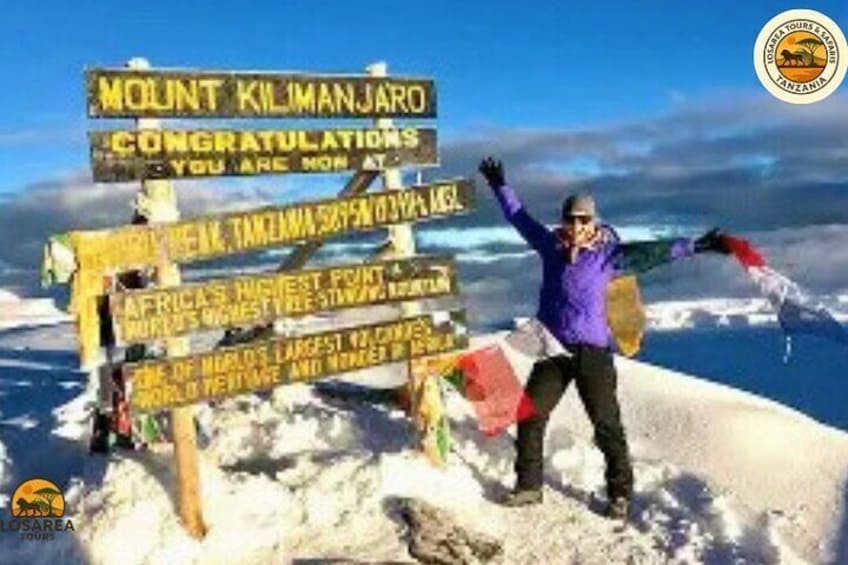 A person standing on a snowy peak with a sign that reads "Mount Kilimanjaro". 2