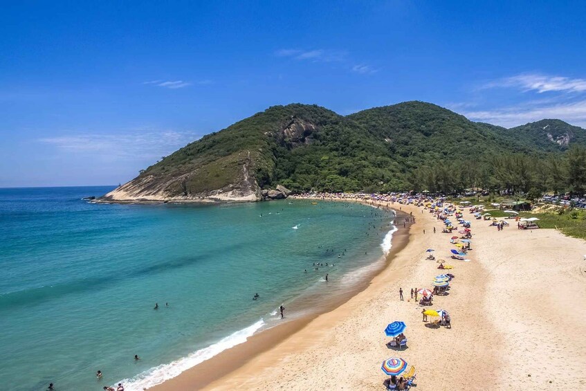 A beach with people swimming and sunbathing, surrounded by green hills. 2