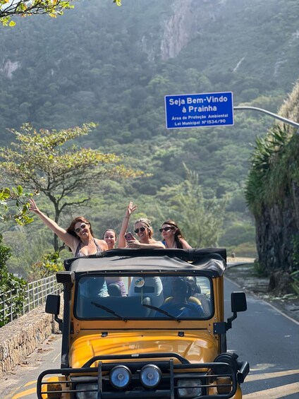 A yellow vehicle with passengers on a road surrounded by greenery and a sign reading "Seja Bem-Vindo à Praia". 3