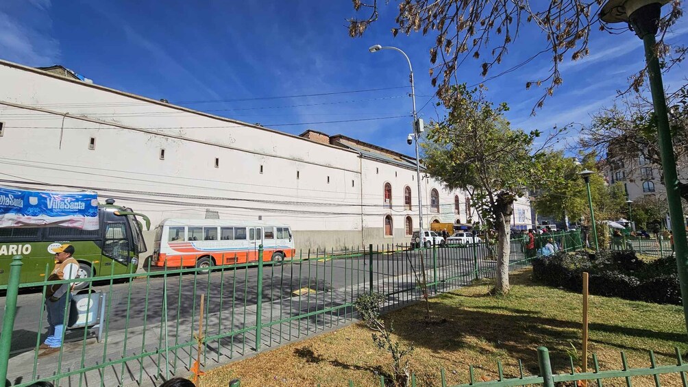 A bus parked on a street, a building, and a fenced garden area. 5