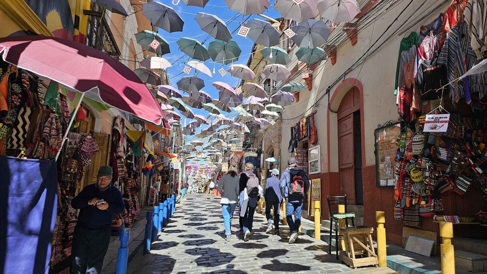 A bustling market street with colorful umbrellas overhead and various shops on either side. 1