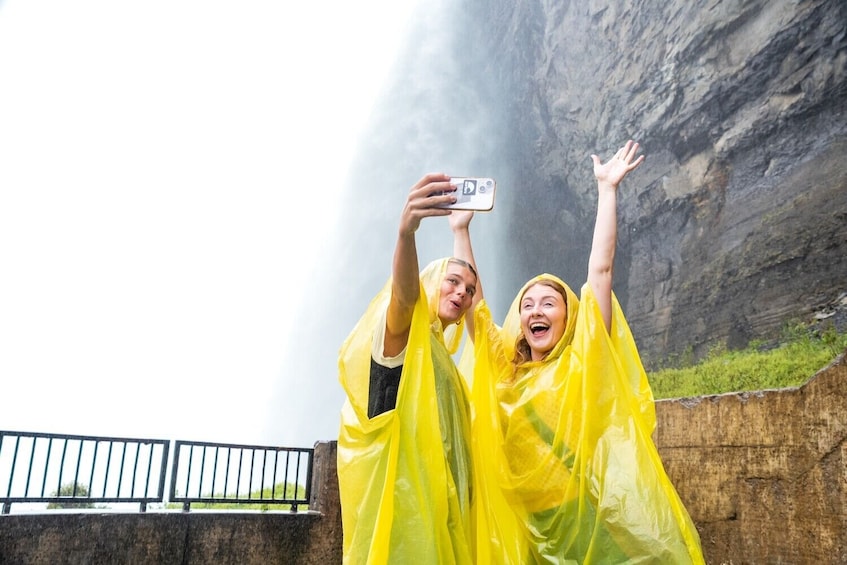 Due persone con impermeabili gialli si fanno un selfie con una scogliera rocciosa sullo sfondo. 1