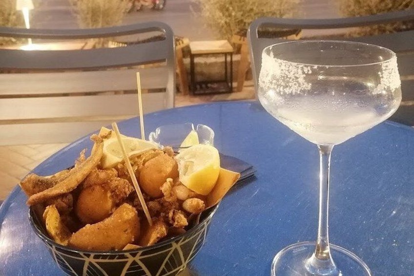 A table with a blue tablecloth, a basket of fried food, and a glass of a clear liquid. 4