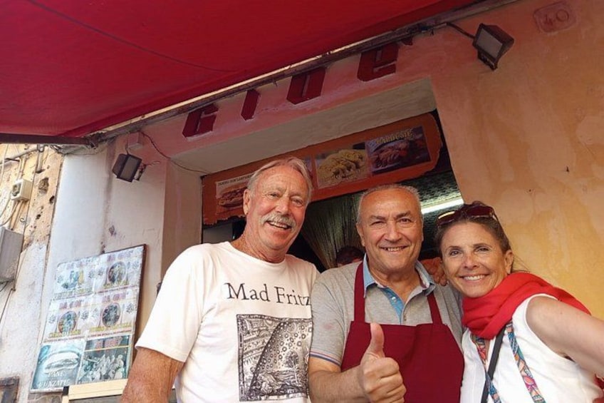 A food truck with a red awning, a man wearing a white t-shirt with a graphic, and another man in a red apron. 5