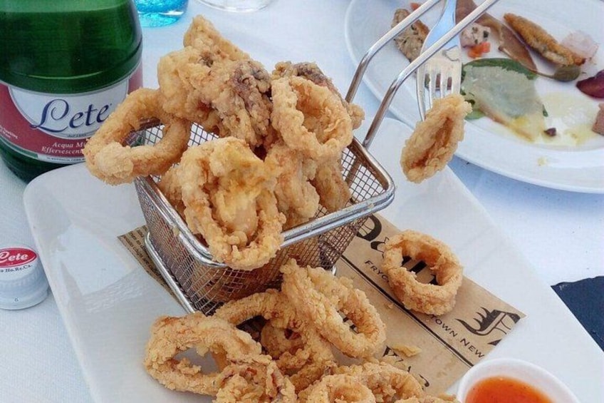 A basket of fried calamari, a bottle of beer, and a plate with food. 3