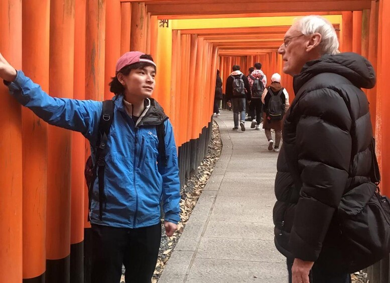 A corridor lined with orange torii gates, a person taking a selfie, and another person in a black jacket. 2