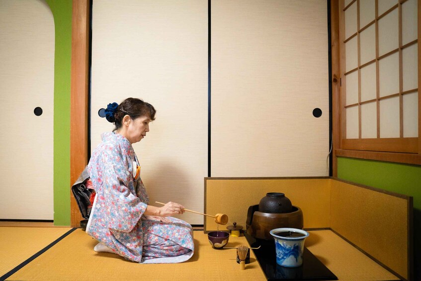 A person in traditional attire performing a tea ceremony with a tea set, including a bowl, whisk, and cup. 1