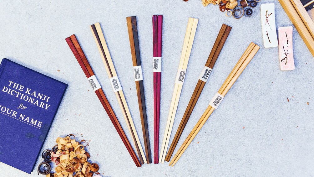 A variety of chopsticks with different colors and wood types, a blue book titled 'The Kanji Dictionary for Your Name,' and some dried flowers. 3