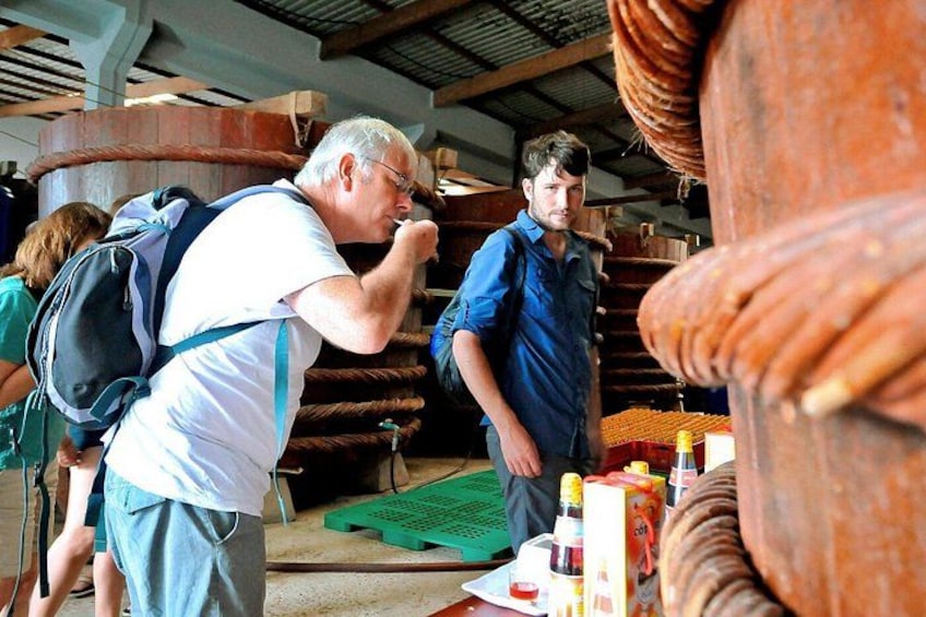A man in a blue shirt and a woman in a green shirt in a workshop with large wooden wheels and tools. 3