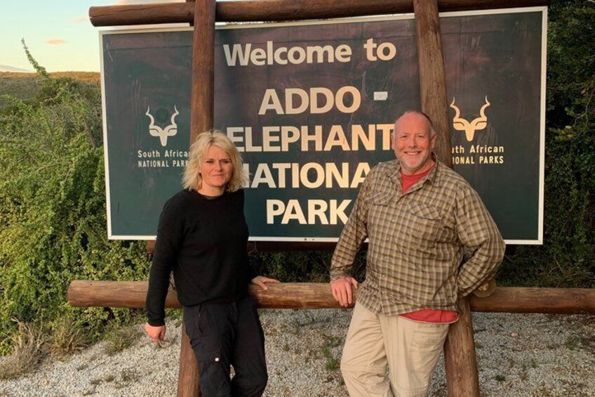 Two people standing in front of a sign for Addo Elephant National Park. 1