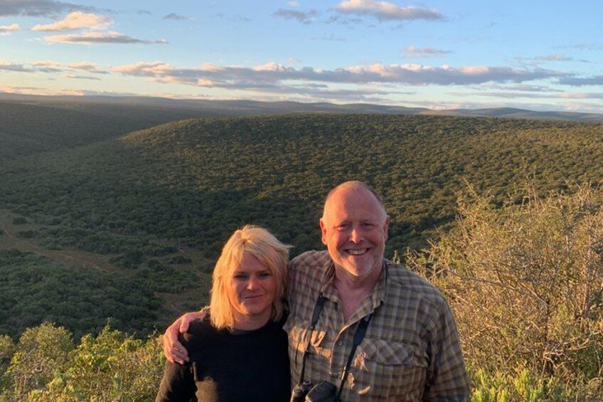 Two people standing on a hill with a forested landscape in the background. 4
