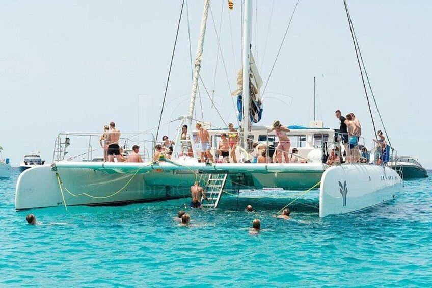 A sailboat with people swimming in the water and standing on the deck. 3