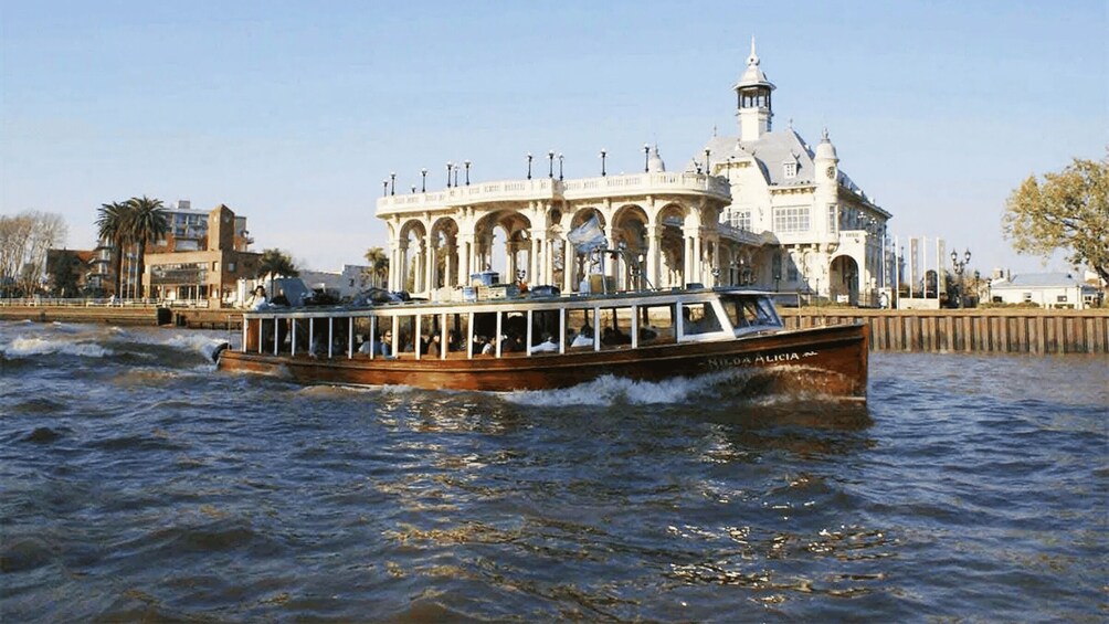 A boat named "Milla Alicia" on a river with a large white building in the background. 1