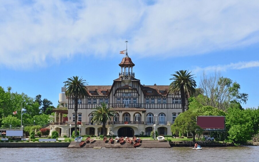 A historic building with a tower, palm trees, and a river. 2