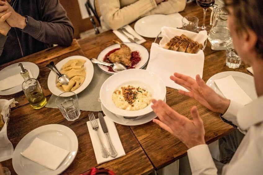 A wooden dining table with plates of food, a bottle of olive oil, and a glass of wine. 1