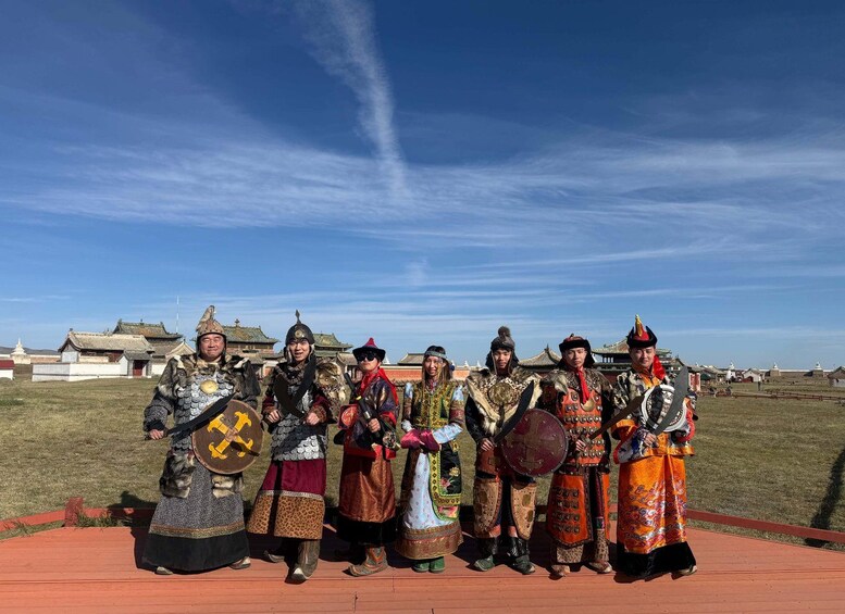A group of people in traditional costumes with shields and weapons, standing on a platform with traditional buildings in the background. 5