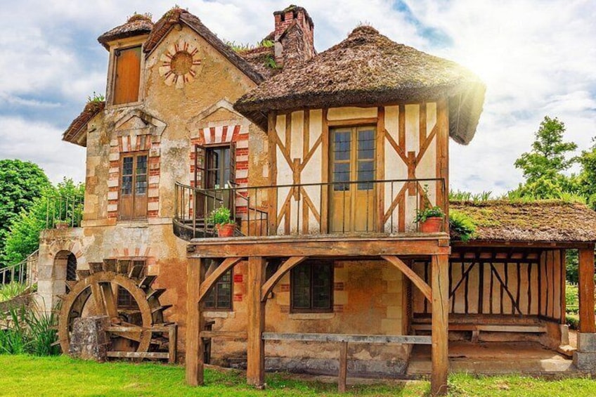 A traditional half-timbered house with a thatched roof, a water wheel, and a balcony with potted plants. 3