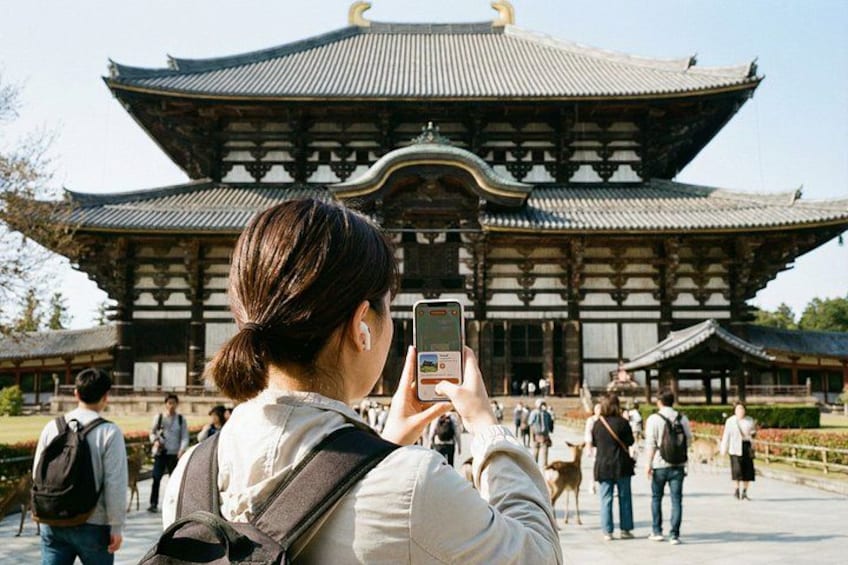 A person taking a photo of a traditional Japanese building with a curved roof and wooden structure. 1