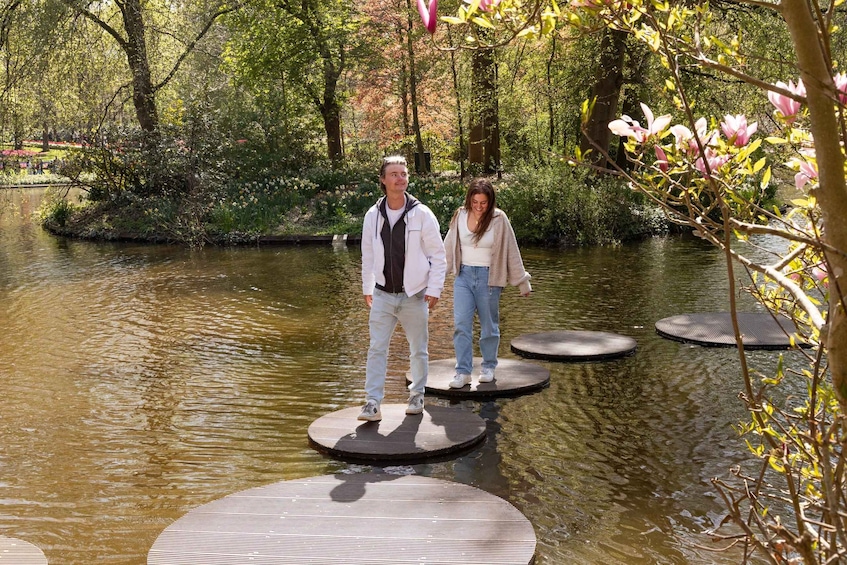 Two people standing on circular floating platforms in a body of water surrounded by trees and flowers. 3
