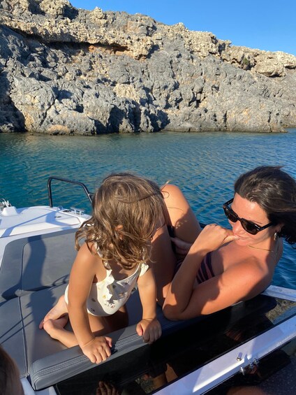 Two people on a boat near rocky cliffs and clear blue water. 1
