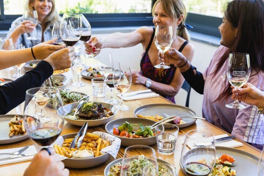 Un grupo de personas brindando con copas de vino alrededor de una mesa llena de diferentes platos. 5