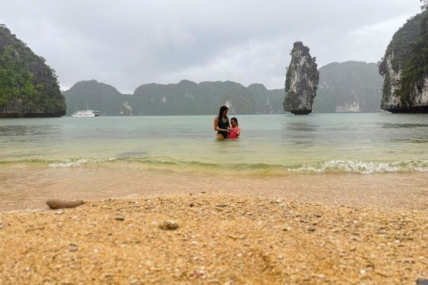 A beach with a person sitting on a red float in the water, surrounded by rocky cliffs and a boat in the distance. 4