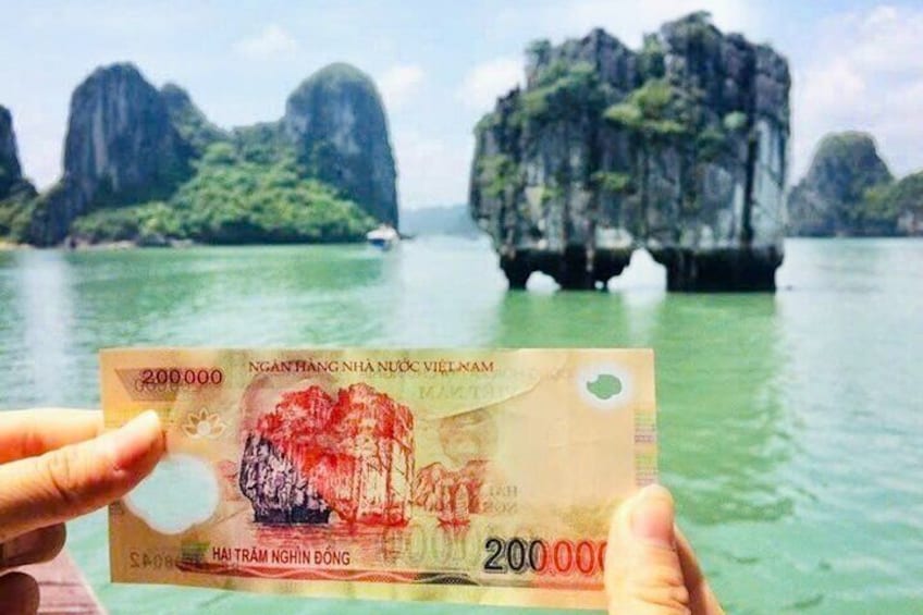 A 200,000 Vietnamese dong note with a red stamp, held in front of a scenic view of limestone karsts in Vietnam. 5