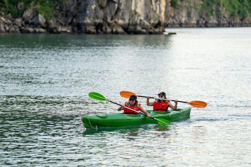 Two people kayaking on calm water with a rocky shoreline in the background. 2