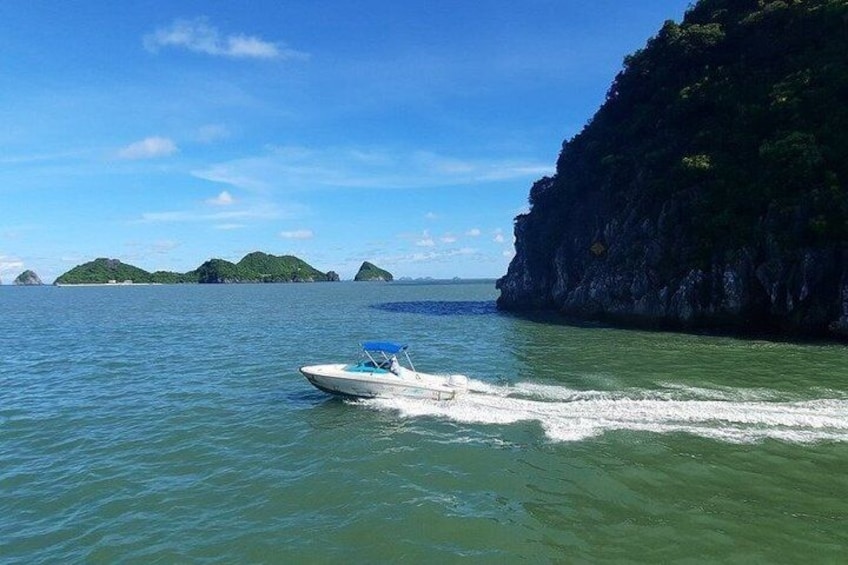 A boat on a calm sea with greenish water, surrounded by rocky cliffs and small islands in the distance. 3