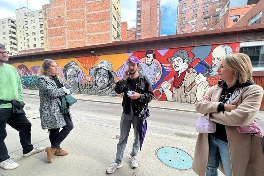 A group of people standing on a city street with a mural in the background. 5