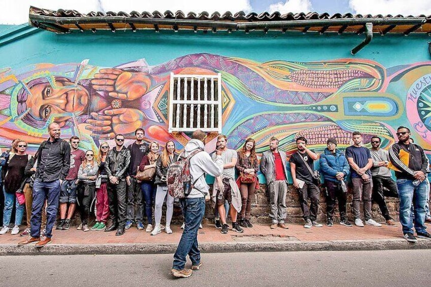 A group of people standing in front of a colorful mural on a building. 1
