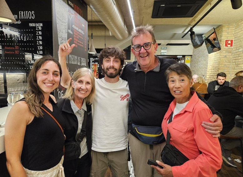 A group of people in a restaurant with a menu board in the background. 1