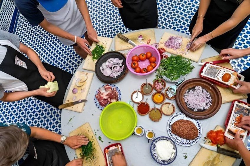 En grupp människor som lagar mat runt ett bord med olika ingredienser och köksredskap. 3