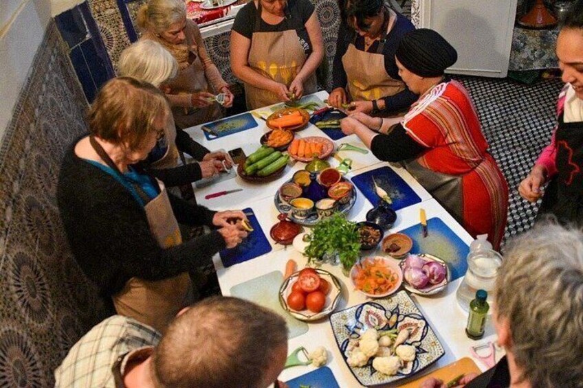 Un gruppo di persone prepara cibo attorno a un tavolo con diverse verdure e piatti. 1