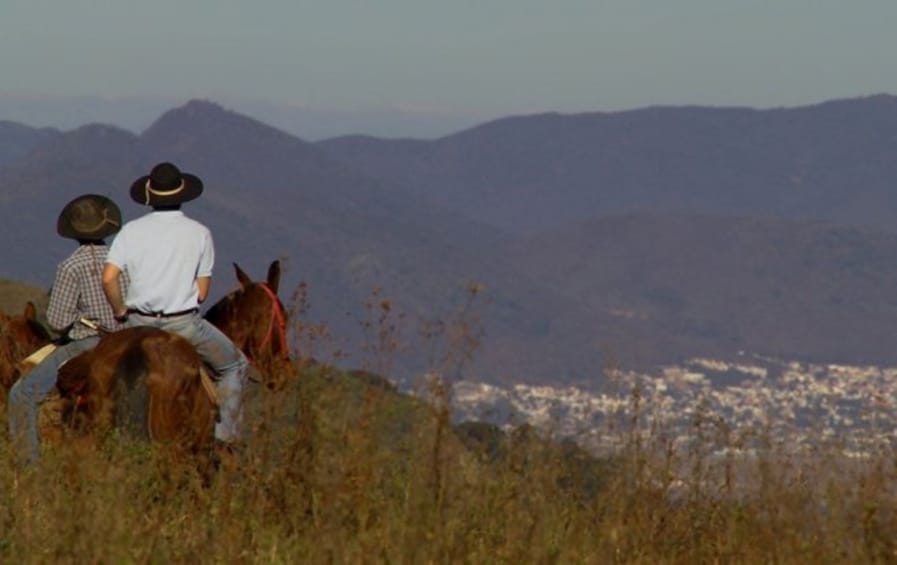 Two people riding horses on a hill overlooking a city. 4