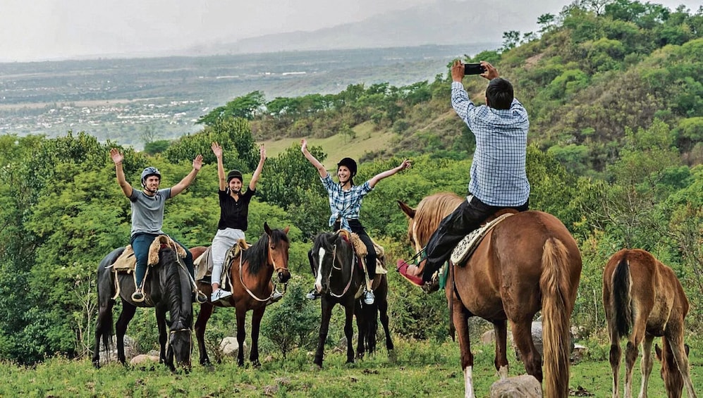 People riding horses on a grassy hill with a scenic view in the background. 3