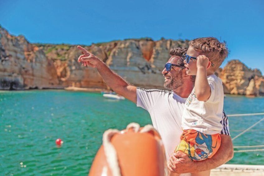 A person holding a child on a boat with a rocky coastline in the background. 2
