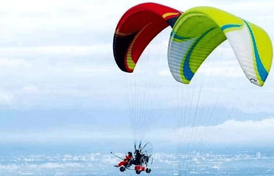 A paraglider with a red and yellow canopy flying over a cityscape. 2