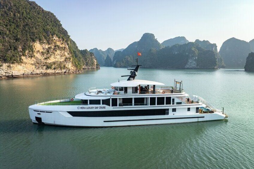 Een witte luxe jacht genaamd HERA LUXURY DAY CRUISE op kalm water, met een bergachtige achtergrond. 2