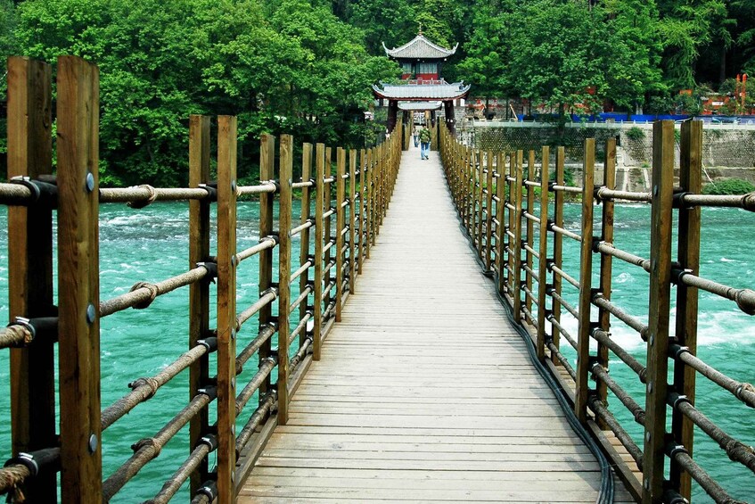A wooden bridge with a traditional pagoda in the distance, surrounded by lush greenery. 1
