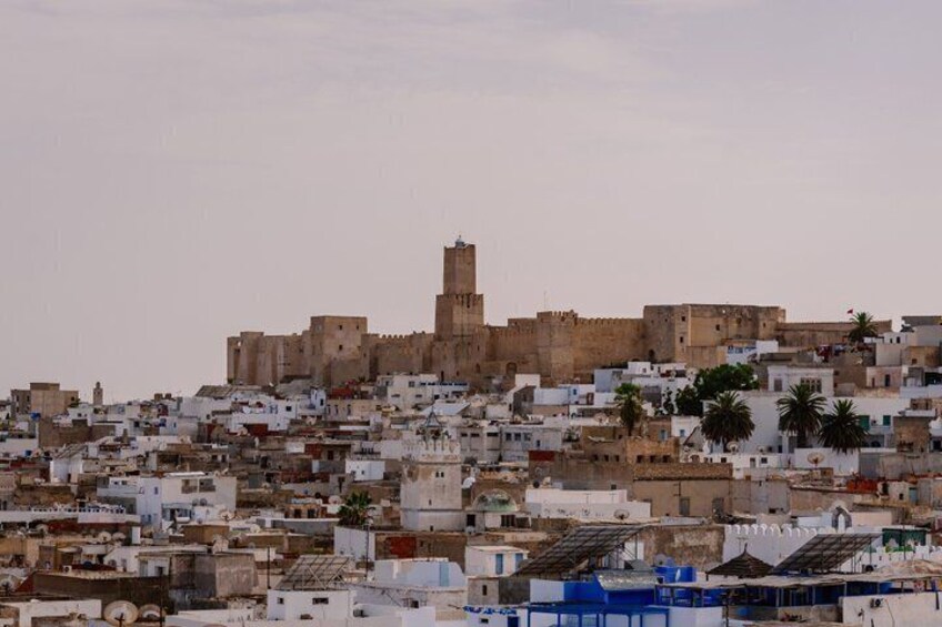A cityscape with a prominent fortress-like structure in the background and densely packed buildings in the foreground. 5