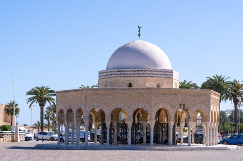 A mosque with a large dome and arches, surrounded by palm trees and cars. 4