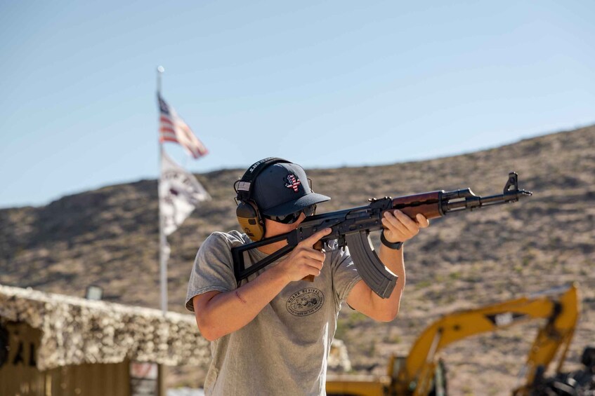 A person aiming a rifle at an outdoor shooting range with an American flag in the background. 5