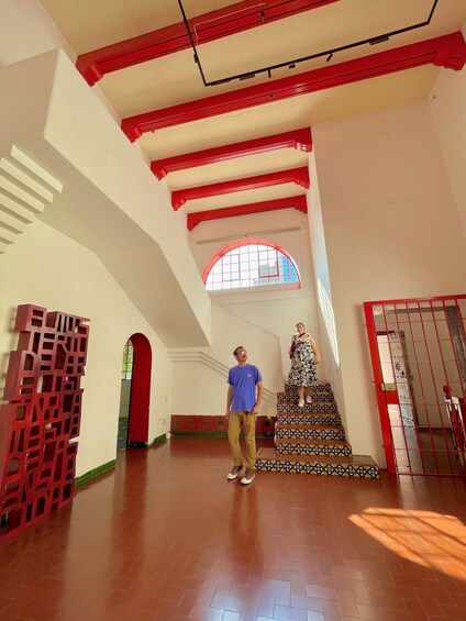 A spacious interior with high ceilings, red beams, and a staircase with patterned tiles. 2