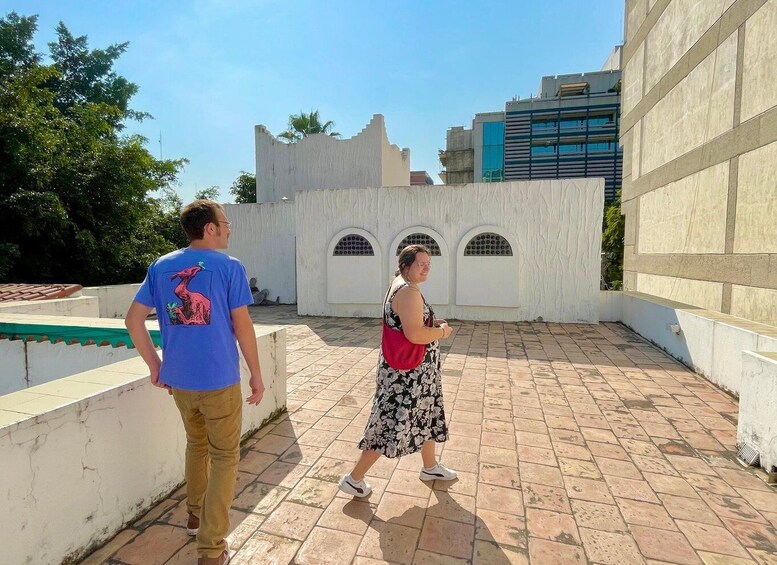Two people walking on a tiled patio with a white wall and arched windows in the background. 5