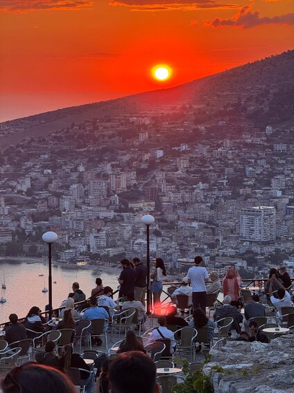 A sunset over a coastal city with people dining at outdoor tables. 2